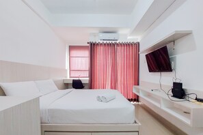 A hotel room with a bed, a desk, a chair, a TV, and an air conditioning unit.