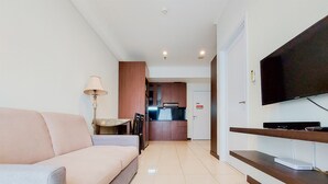 A modern living room with a sofa, a flat-screen TV mounted on the wall, and a kitchen area in the background. - Elegant And Tidy 1Br Apartment Silkwood Residences (Tangerang)