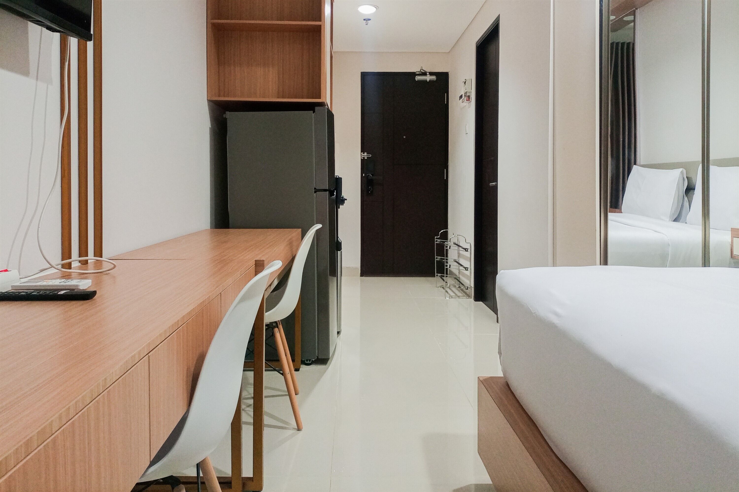 A hotel room with a wooden desk, white chairs, a bed, and a dark door.