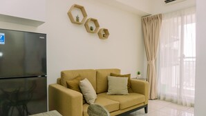 A living room with a beige sofa, a black refrigerator, and hexagonal wall decorations. - Well Furnished 2Br Apartment M-Town Residence Near Mall (Gading Serpong)