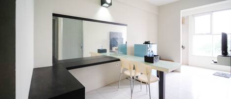 A modern, minimalist room with a black console table, a glass dining table with two chairs, a large mirror, and a small TV on a stand.