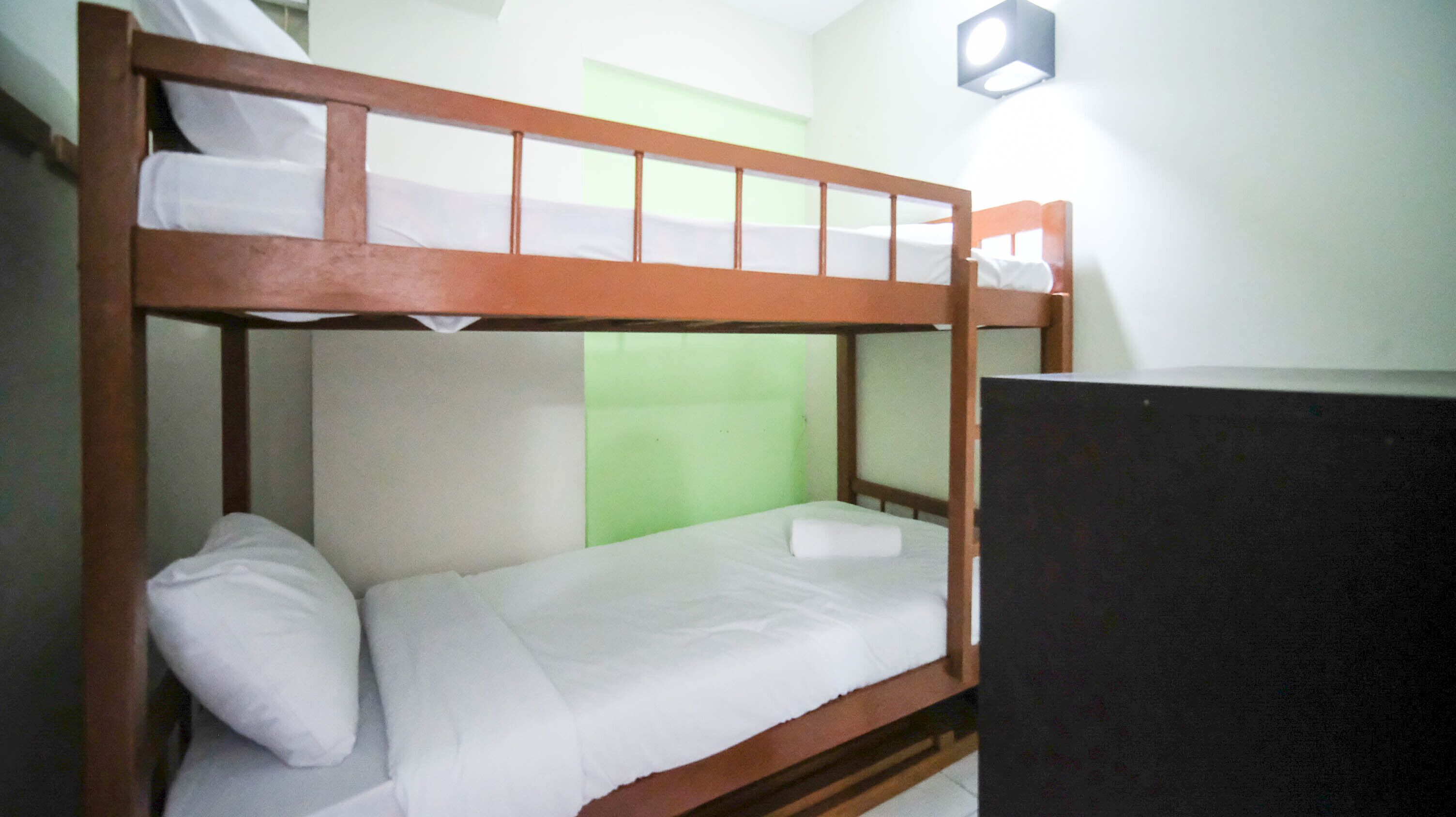 Un letto a castello con una partizione verde, un comodino e un portalampada fissato alla parete.