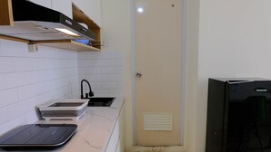A modern kitchen with white tiles, a black countertop, a sink, and a Panasonic refrigerator. - Cozy And Homey 2Br Tamansari Panoramic Apartment (Bandung)