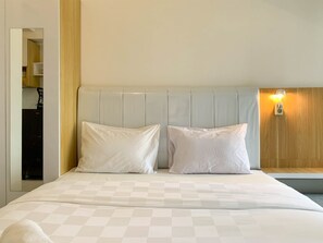Quarto de hotel com uma cama grande, duas almofadas, cabeceira, mesa de cabeceira e luz acoplada à parede.