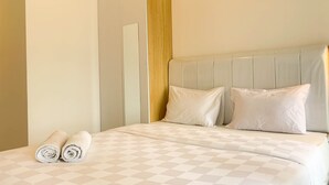 A neatly made bed with a checkered bedspread, two pillows, and rolled towels on the side. - Restful And Cozy Studio Tokyo Riverside Pik 2 Apartment (Teluknaga)