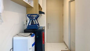 A narrow hallway with a white door, a small shelf with a phone, and a blue object on a black surface. - Restful And Cozy Studio Tokyo Riverside Pik 2 Apartment (Teluknaga)