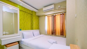 Ein Hotelzimmer mit Bett, Nachttisch, Spiegel, einem Fenster mit Vorhängen und einer Klimaanlage.