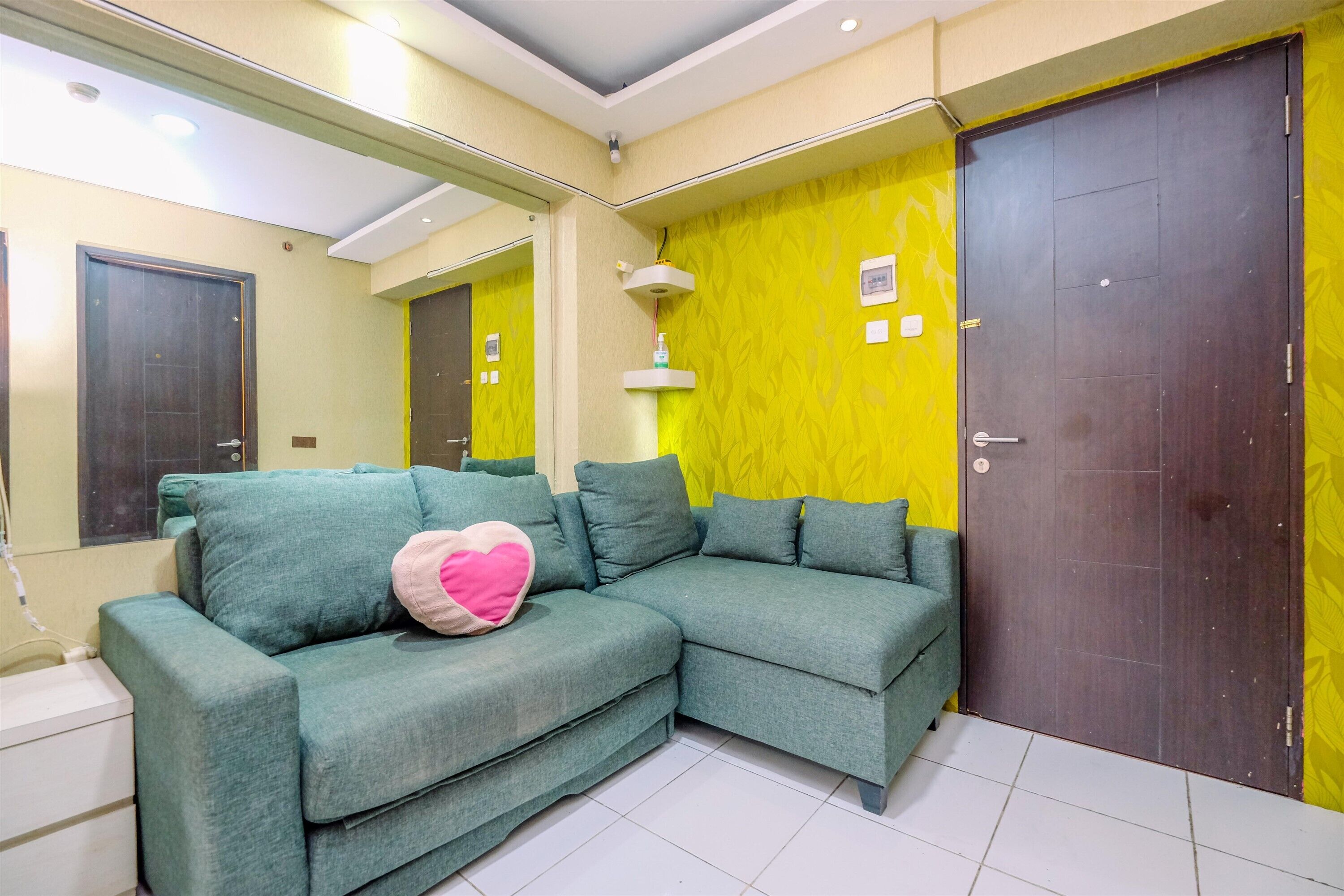 A room with a green sofa, a heart-shaped pillow, a mirror, and a yellow wall.