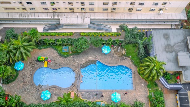 Ein Luftbild eines Wohnhauses mit Schwimmbad, Palmen und einem Spielplatz.