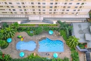 An aerial view of a residential building with a swimming pool, palm trees, and a playground. - Nice And Modern 2Br At Kebagusan City Apartment (Jakarta)