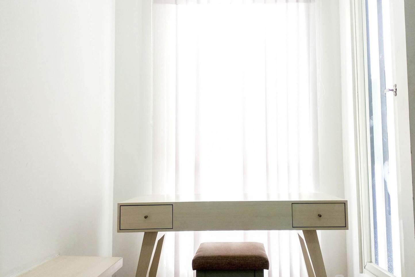 Ein Zimmer mit Fenster, Schreibtisch mit Schubladen und einer Bank.