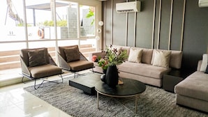 A modern living room with a sofa, two armchairs, a coffee table, and a large window with a view of greenery. - Modern Studio At Barsa City Apartment (Yogyakarta)