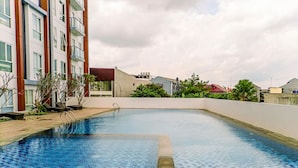 A rooftop swimming pool with a tiled edge, surrounded by a low brick wall and a building with multiple floors and balconies. - Modern Studio At Barsa City Apartment (Yogyakarta)