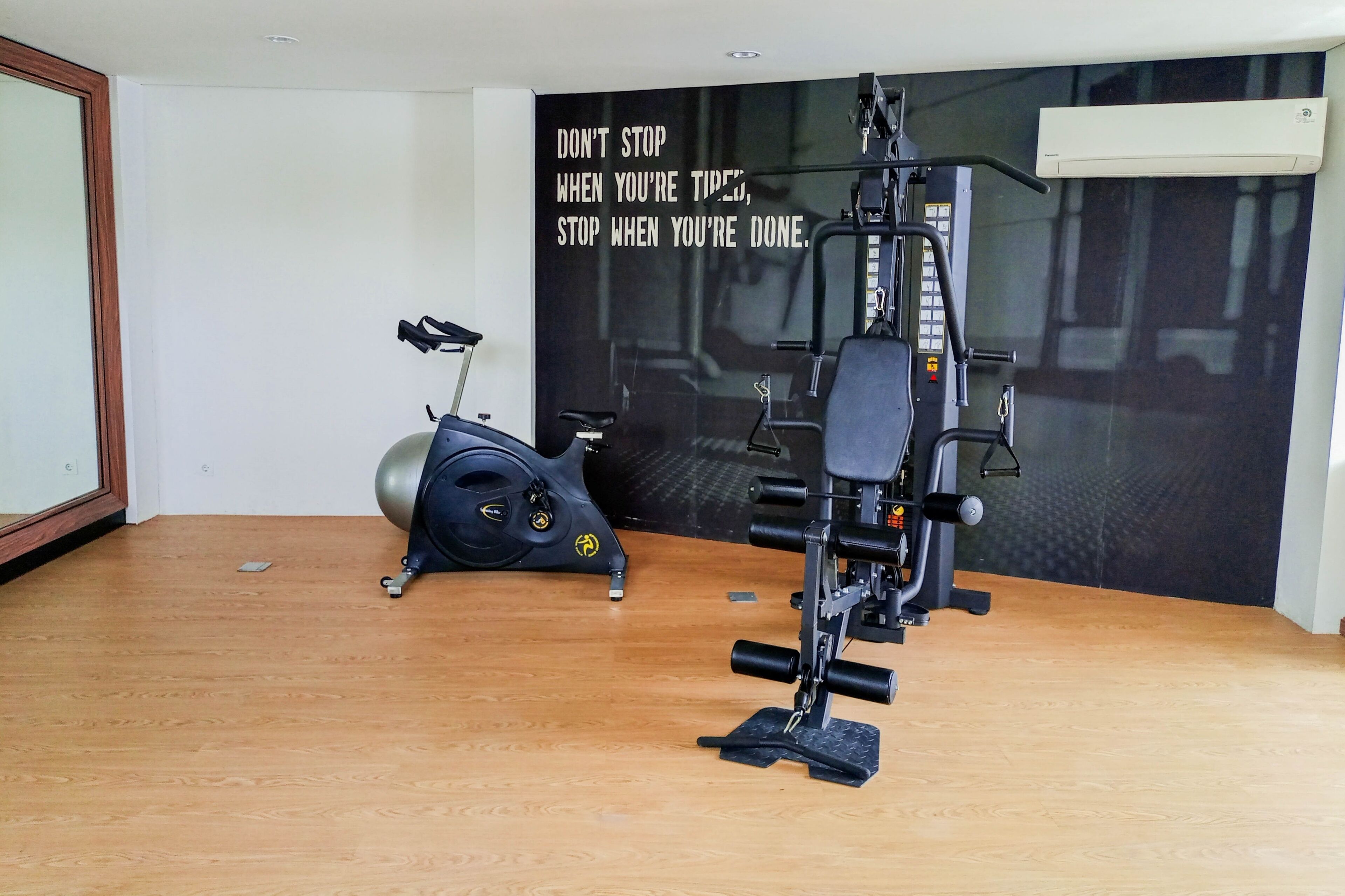 A home gym with a stationary bike, a weight bench, and a large motivational poster on the wall.