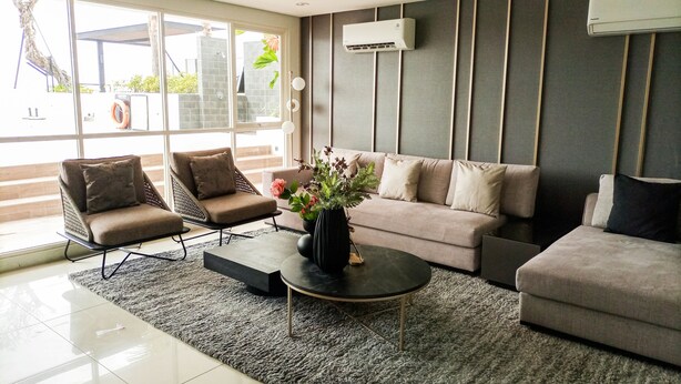 Un salon moderne comprenant un canapé, deux fauteuils, une table basse et une grande fenêtre avec un appareil de climatisation.