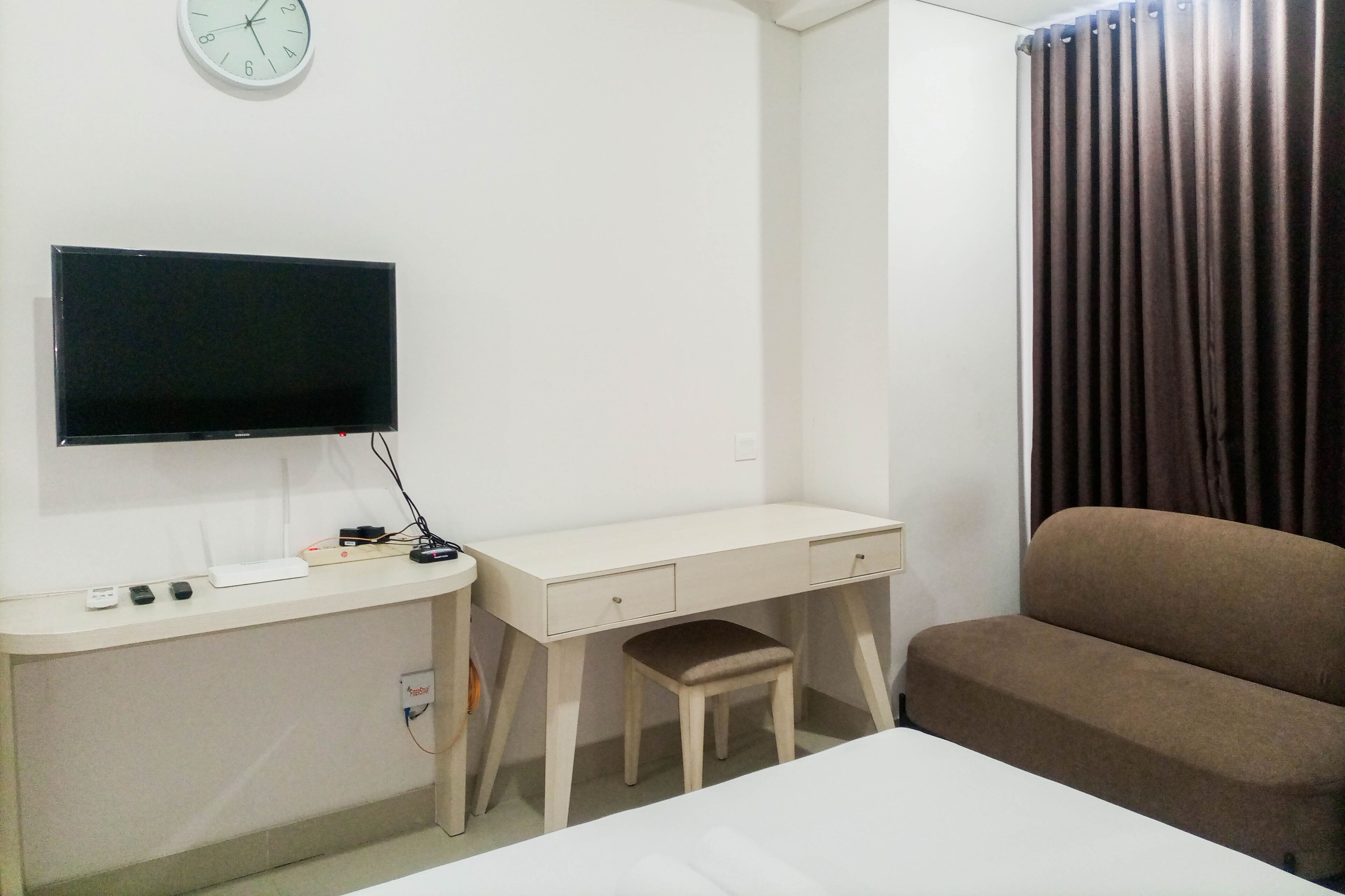 A hotel room with a bed, a desk with a chair, a television, and a window with curtains.