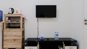 A room with a wooden cabinet, a black TV on the wall, and a black table with two drawers. - Good Deal 1Br Apartment At Parahyangan Residence (Bandung)