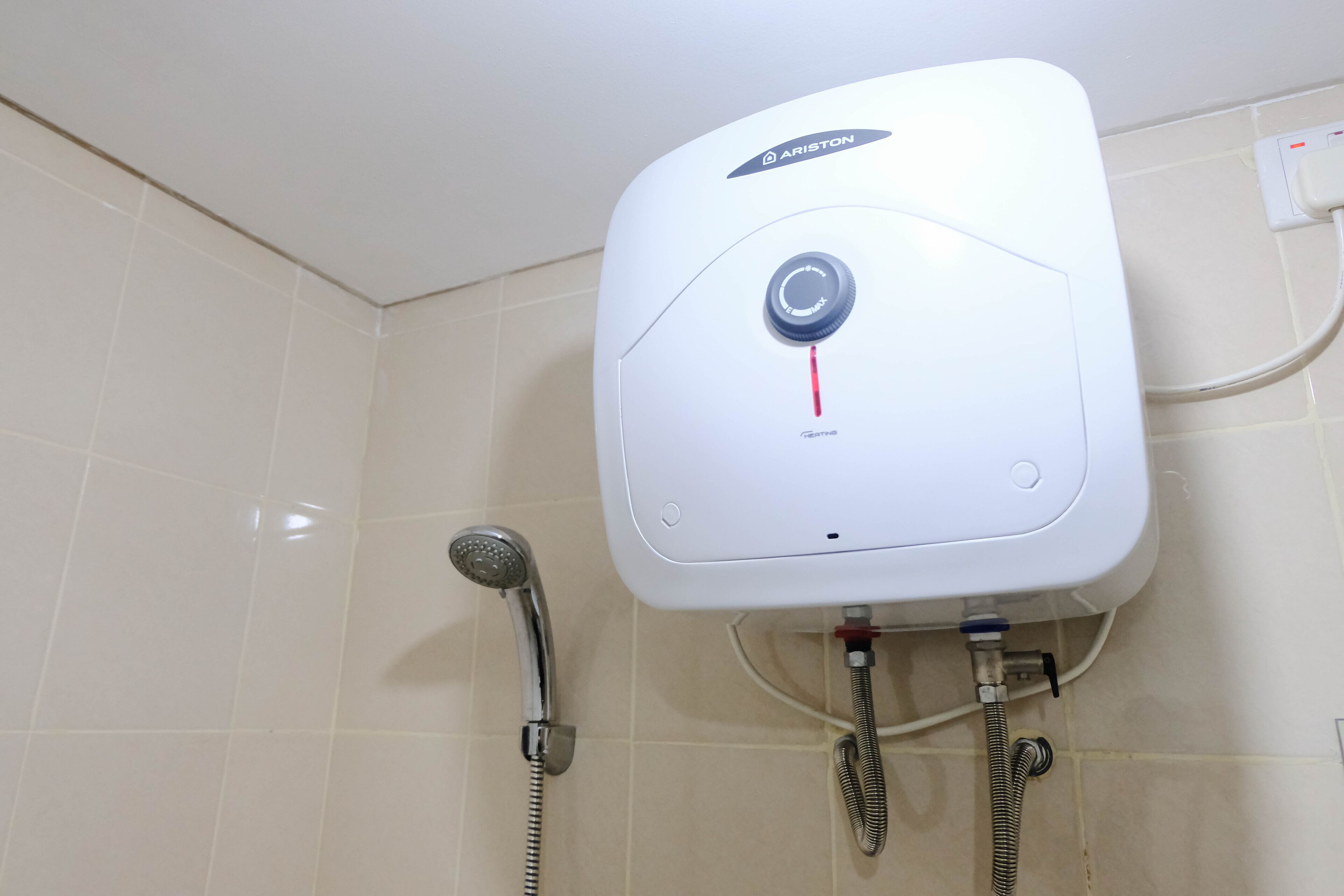 Eine an der Wand befestigte Duscharmatur mit Drehregler, einer Handbrause und zwei flexiblen Schläuchen.
