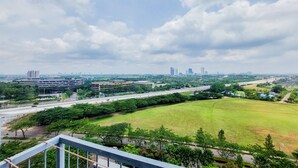 Un paisaje urbano con un amplio campo verde, edificios y una autopista.