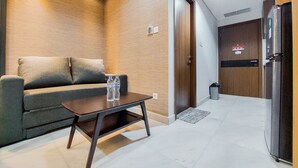 Una sala moderna con un sofá gris, un muro de acento de madera, una pequeña mesa con dos botellas de agua y una puerta que da a una cocina.