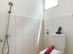 Un baño con paredes de azulejos blancos, una ducha con manguera, un inodoro y una ventana.