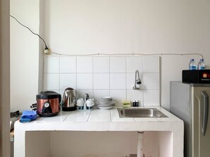 Una cocina con azulejos blancos, un lavamanos, una cafetera, un hervidor y un refrigerador.