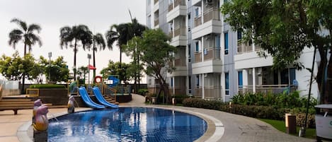 Ein Schwimmbad mit Wasserrutschen, umgeben von einem Gebäude mit Balkonen und Palmen.
