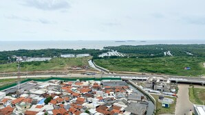 Une ville côtière où se côtoient des bâtiments résidentiels et industriels, un espace vert arboré et une vue sur la mer, avec des navires visibles au loin.