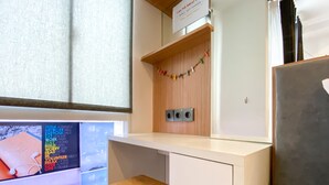 Une petite pièce moderne, dotée d’un bureau en bois, d’un tabouret et d’une fenêtre donnant sur le ciel.