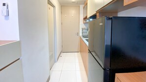 Une cuisine étroite avec des meubles blancs, un réfrigérateur noir et une porte donnant sur une autre pièce.