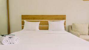 A neatly made bed with white linens and pillows, a wooden headboard, and a rolled towel on the side.