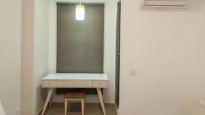 Pieni, siisti huone, jossa on yksi työpöytä, tuoli, riippuvalaisin ja seinälle asennettu ilmastointilaite.