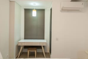 Compact room with a single desk, air conditioning unit, and stool.