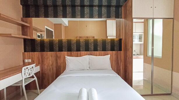 A hotel room with a bed, a desk, and a chair. There is a bathroom visible through a glass door. - Classic Studio At Student Castle Yogyakarta Apartment (Depok)