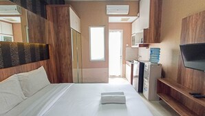 A hotel room with a large bed, a TV, a minibar, and a water dispenser. - Classic Studio At Student Castle Yogyakarta Apartment (Depok)