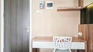 A room with a wooden desk, a white chair, a door, and a wall-mounted shelf. - Classic Studio At Student Castle Yogyakarta Apartment (Depok)