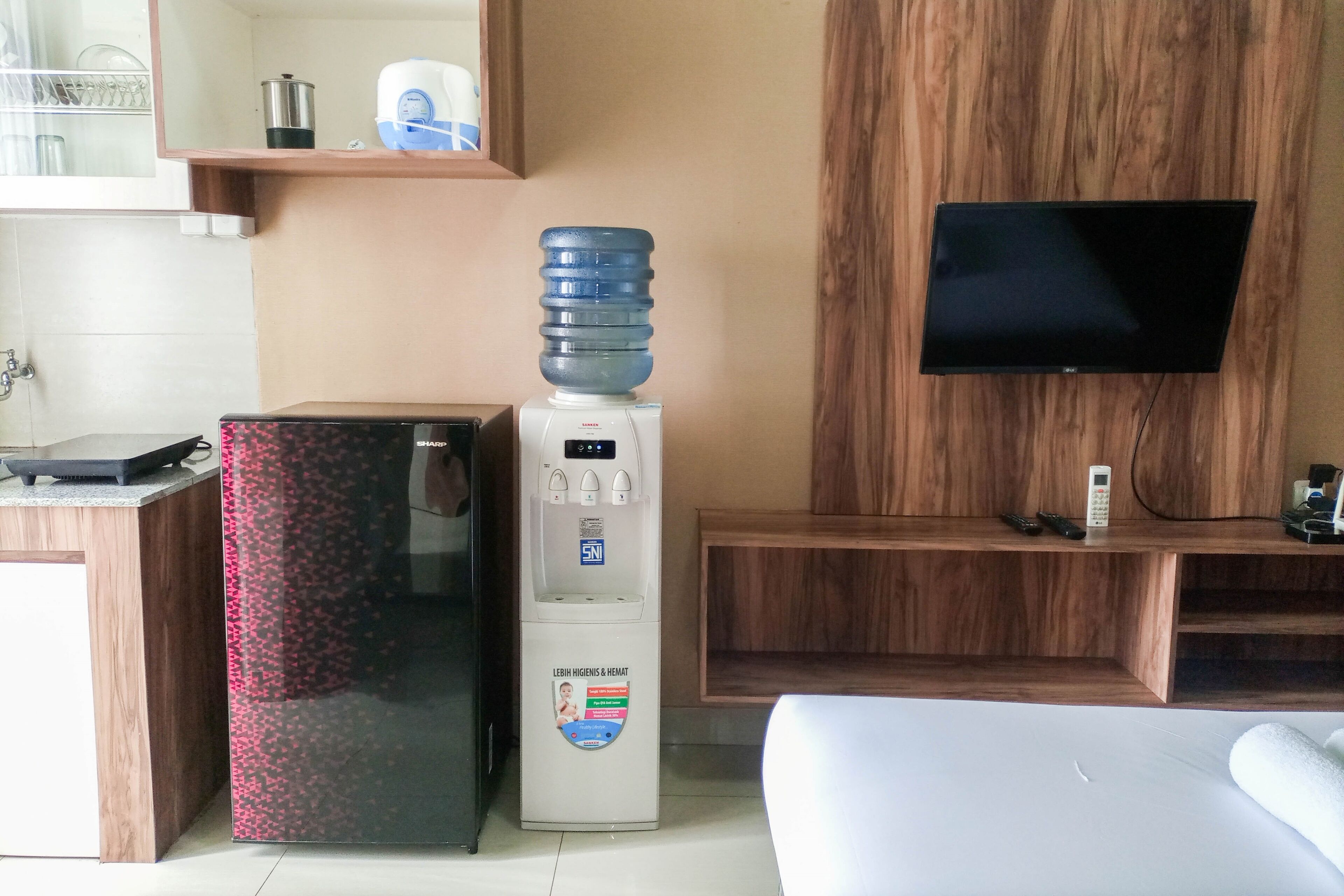 Ett hotellrum med en minibar, en vattenautomat, en tv och en säng.