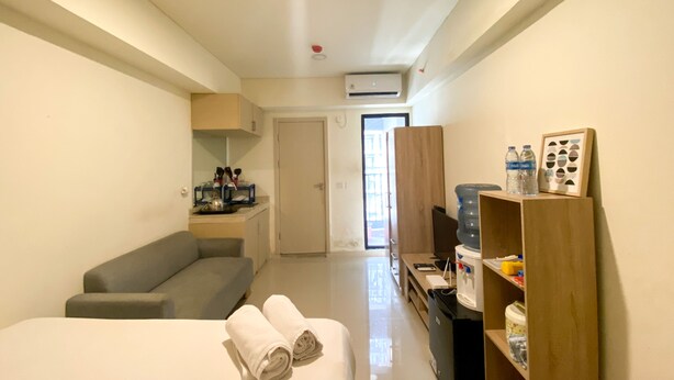 A compact hotel room with a bed, a grey sofa, a small kitchenette, and a water dispenser.