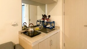 A compact kitchen with a countertop, a kettle, a sink, and a mirror above it.
