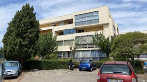 Ein mehrstöckiges Gebäude mit Parkplatz, mehreren parkenden Autos und einem großen Baum.