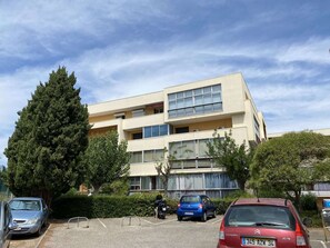 Un edificio a più piani con un parcheggio antistante, diverse auto parcheggiate e un albero di grandi dimensioni.