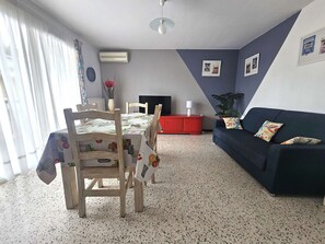 Un coin repas avec une table et des chaises, un buffet rouge, un canapé foncé et une plante.