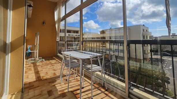 Ein Balkon mit Tisch und Stühlen, großen Fenstern und Blick auf Gebäude.
