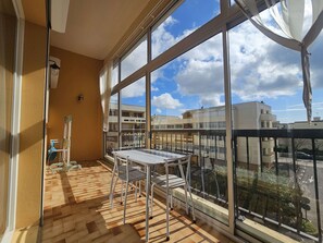 Un balcon avec une table et des chaises, de grandes fenêtres et une vue sur les immeubles.