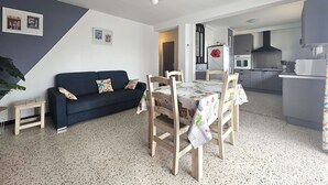 Ein kompakter Wohnbereich mit Sofa, Esstisch, Stühlen, Küchenzeile und einer Deckenleuchte.