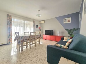 A living room with a sofa, a TV, a dining table with chairs, and a red cabinet. - Spacious 2-Bedroom Apartment with Garage, Loggia & Wifi - 3-Star Rating (Balaruc-les-Bains)