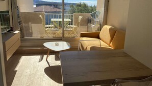 A balcony with a view of buildings and trees, a yellow sofa, a small table, and a wooden floor. - T1 Loft with Air Conditioning, Parking and Wifi in Balaruc-les-Bains (Balaruc-les-Bains)