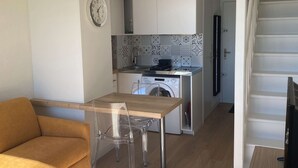 A compact kitchen with a washing machine, a dining area with a sofa and chairs, and a clock on the wall. - T1 Loft with Air Conditioning, Parking and Wifi in Balaruc-les-Bains (Balaruc-les-Bains)