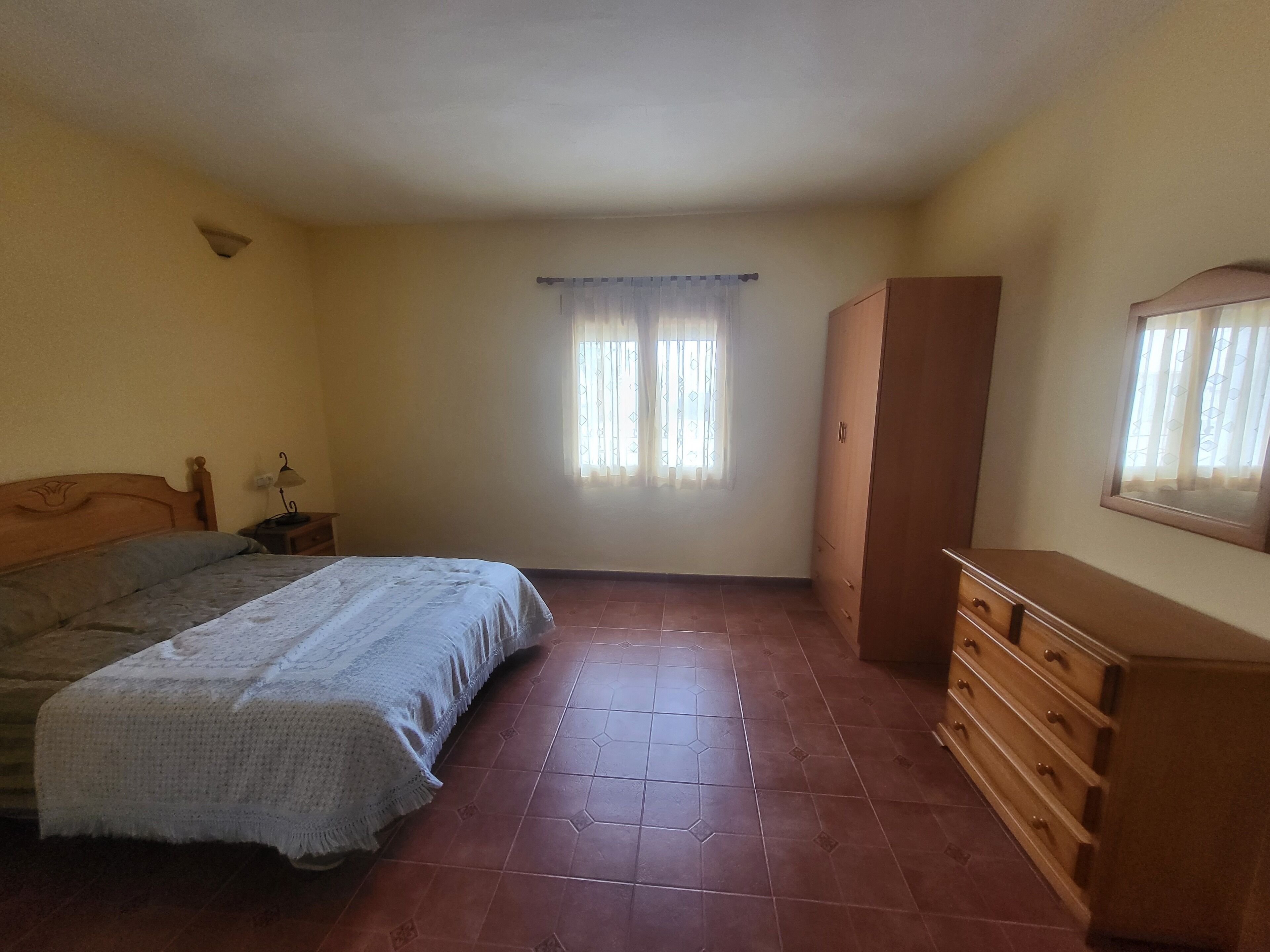 A bedroom with a bed, a dresser, a wardrobe, and a window with curtains.