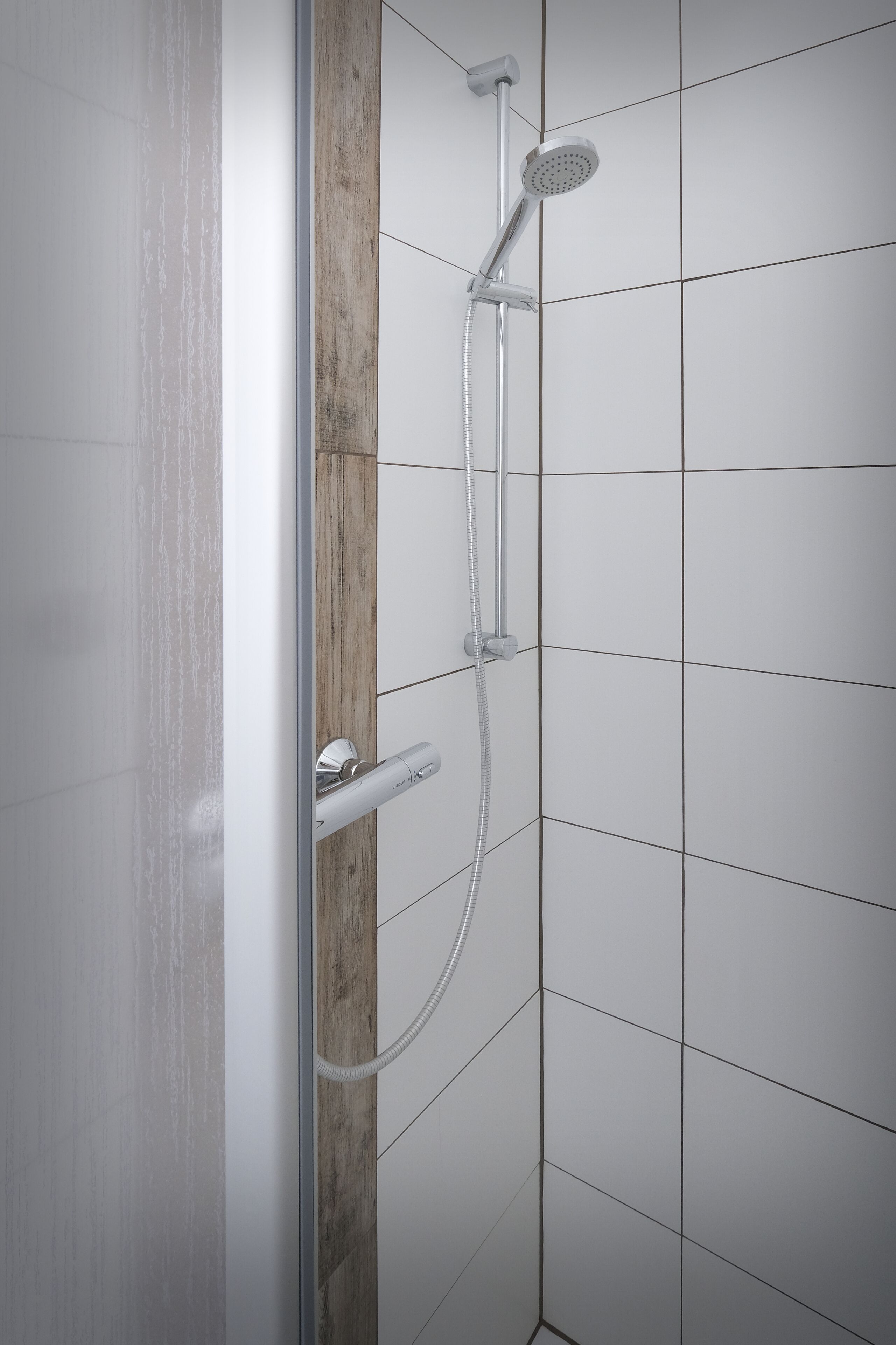 A shower with a handheld showerhead and a wall-mounted control panel.